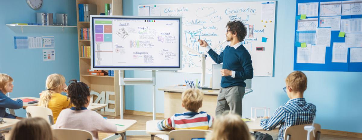 Elementary School Science Teacher Uses Interactive Digital Whiteboard to in front of a Classroom Full of Children 